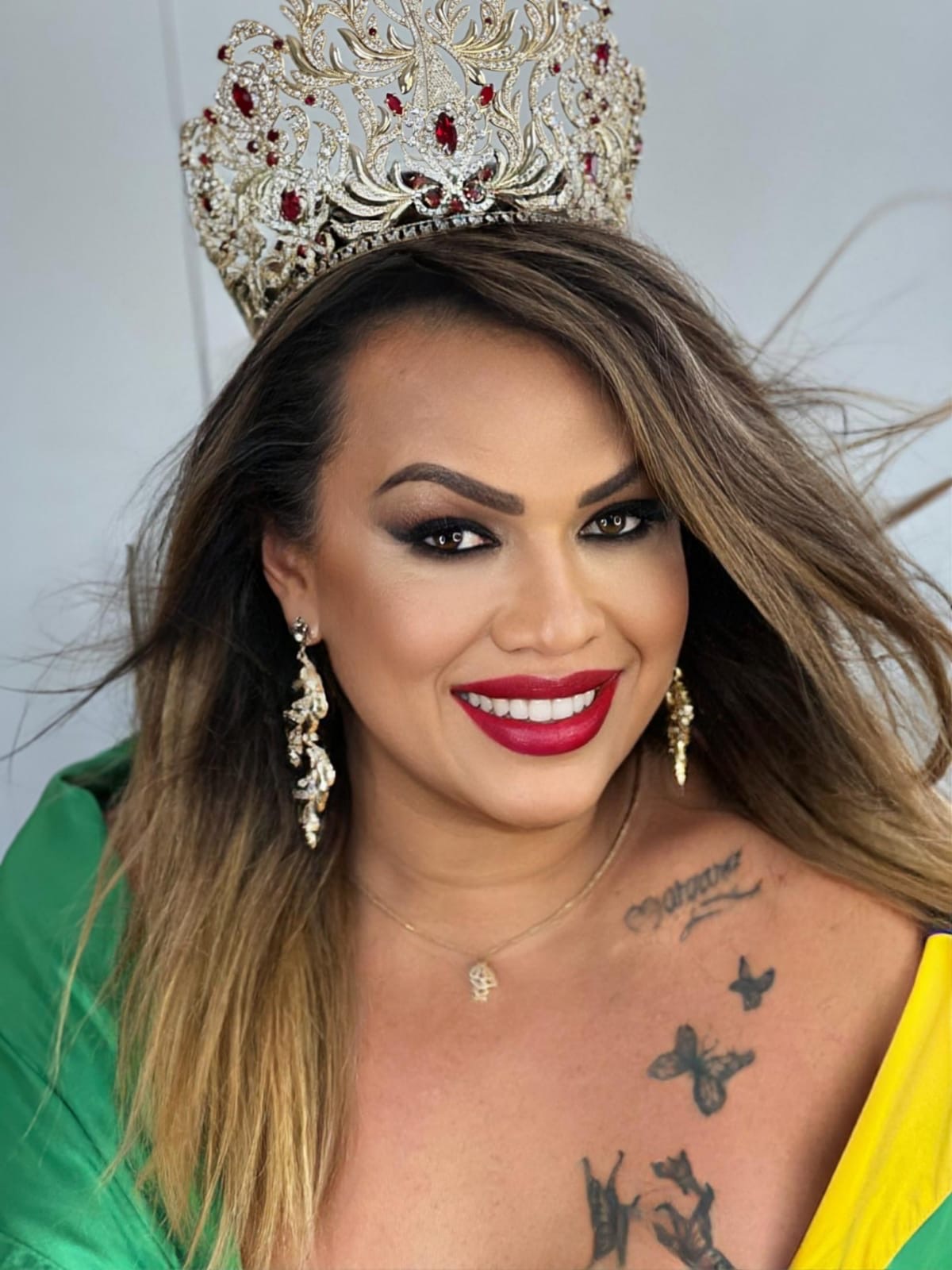Close-up de uma Miss Universe Trans Brasil sorrindo, com coroa e faixa, transmitindo confiança e alegria.