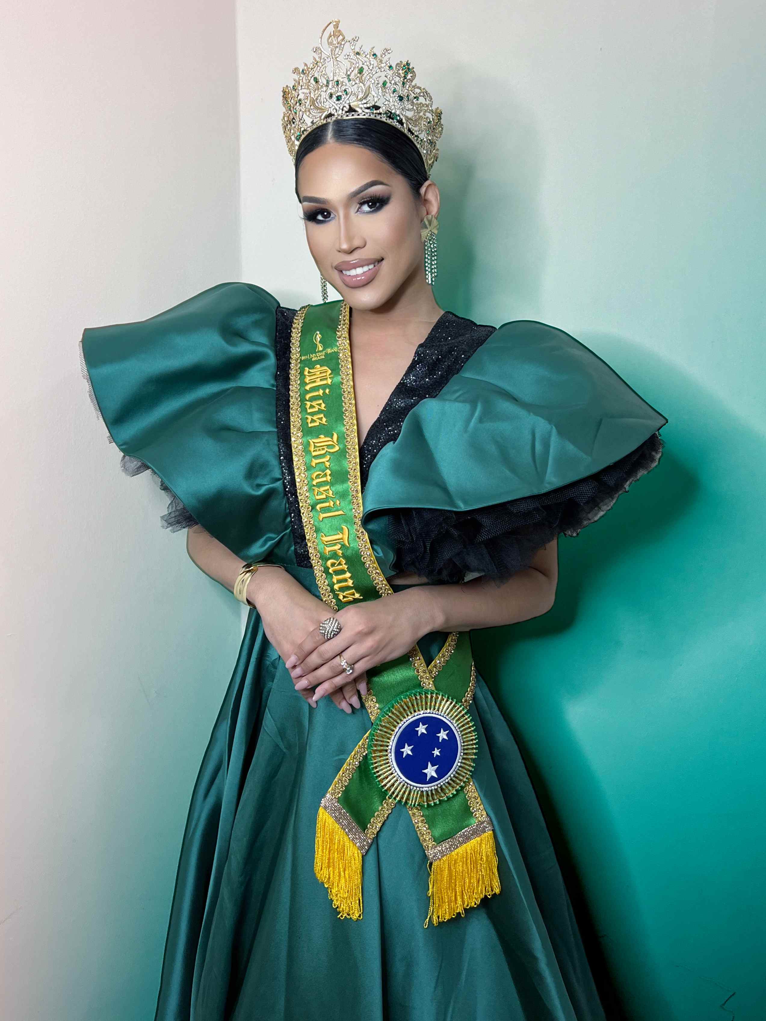 Miss Brasil Trans em um vestido verde com grandes mangas e coroa.