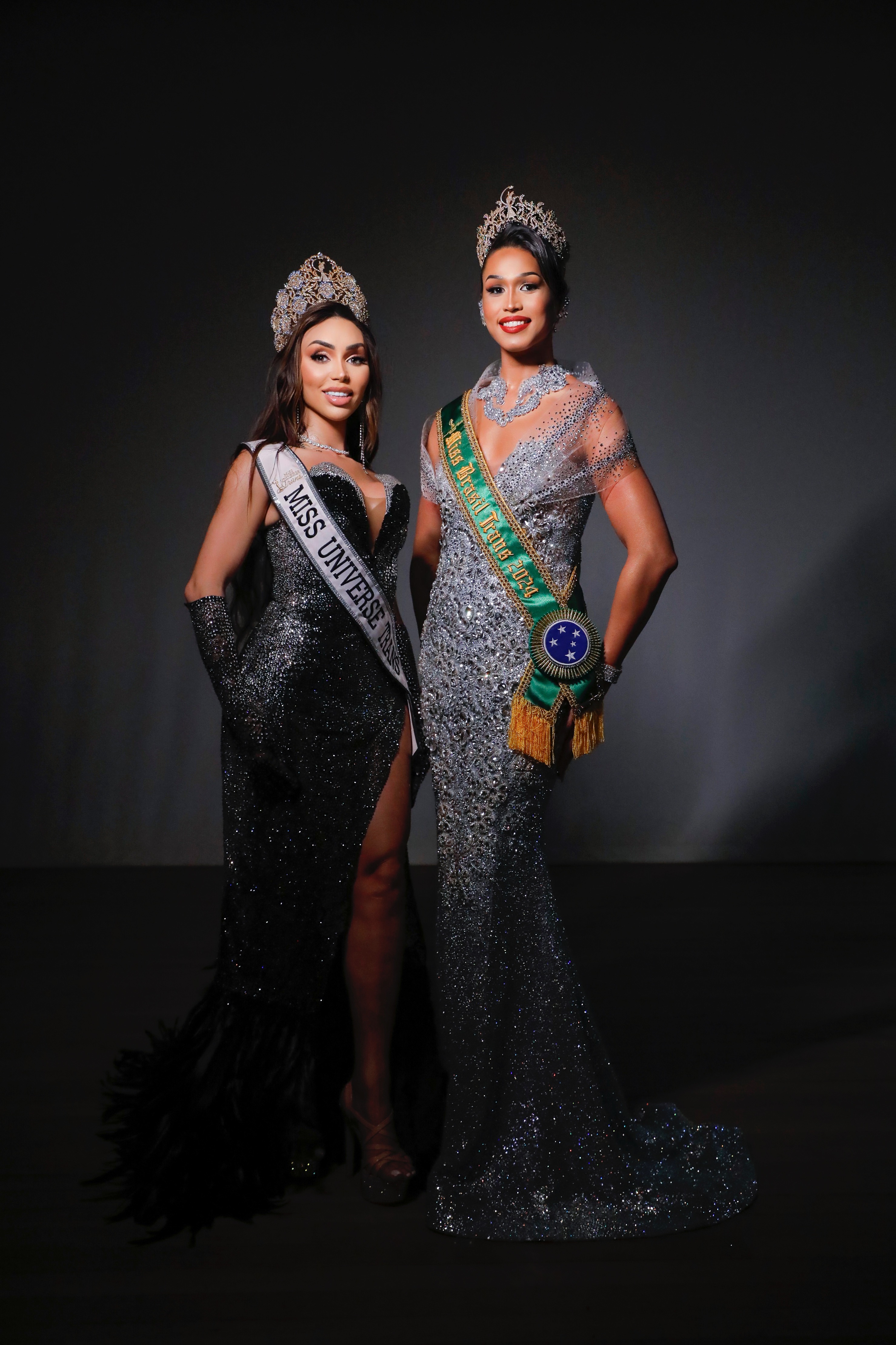 Duas Miss Universe Trans Brasil em vestidos de gala, com coroas e faixas, representando a beleza e a diversidade.